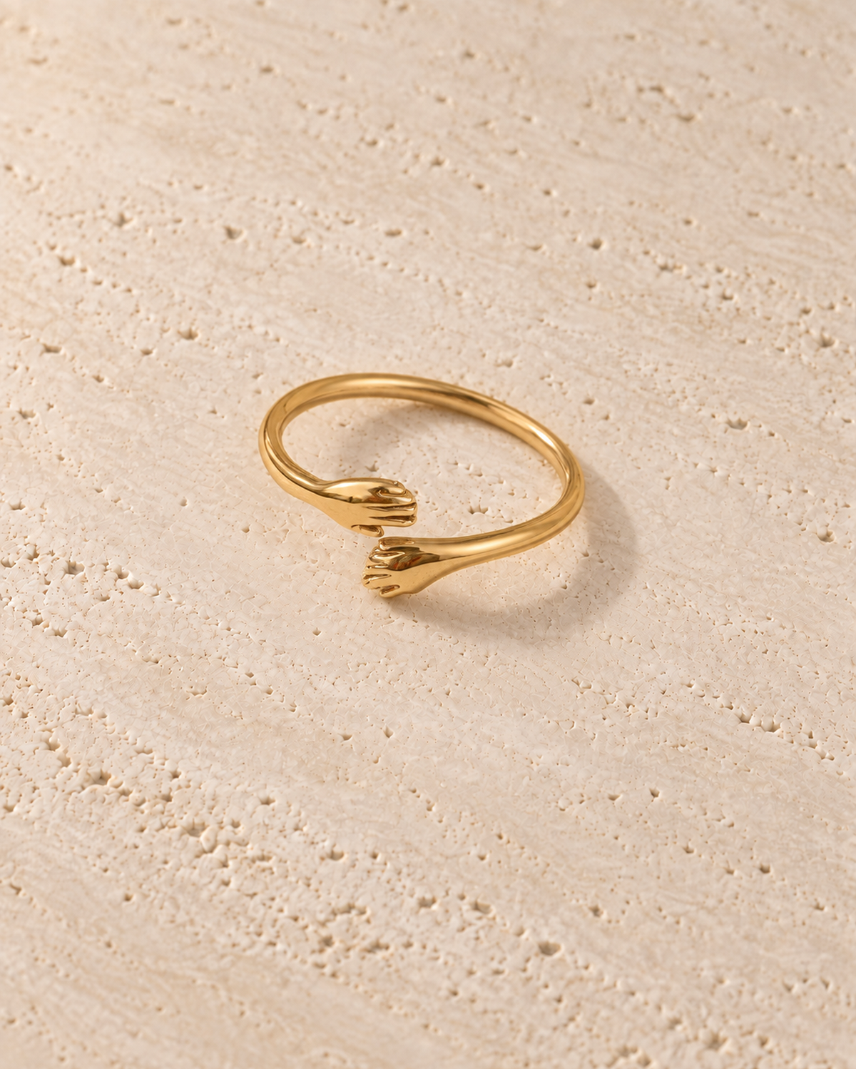 Abbraccio Hug Ring in goudkleur op warm travertin