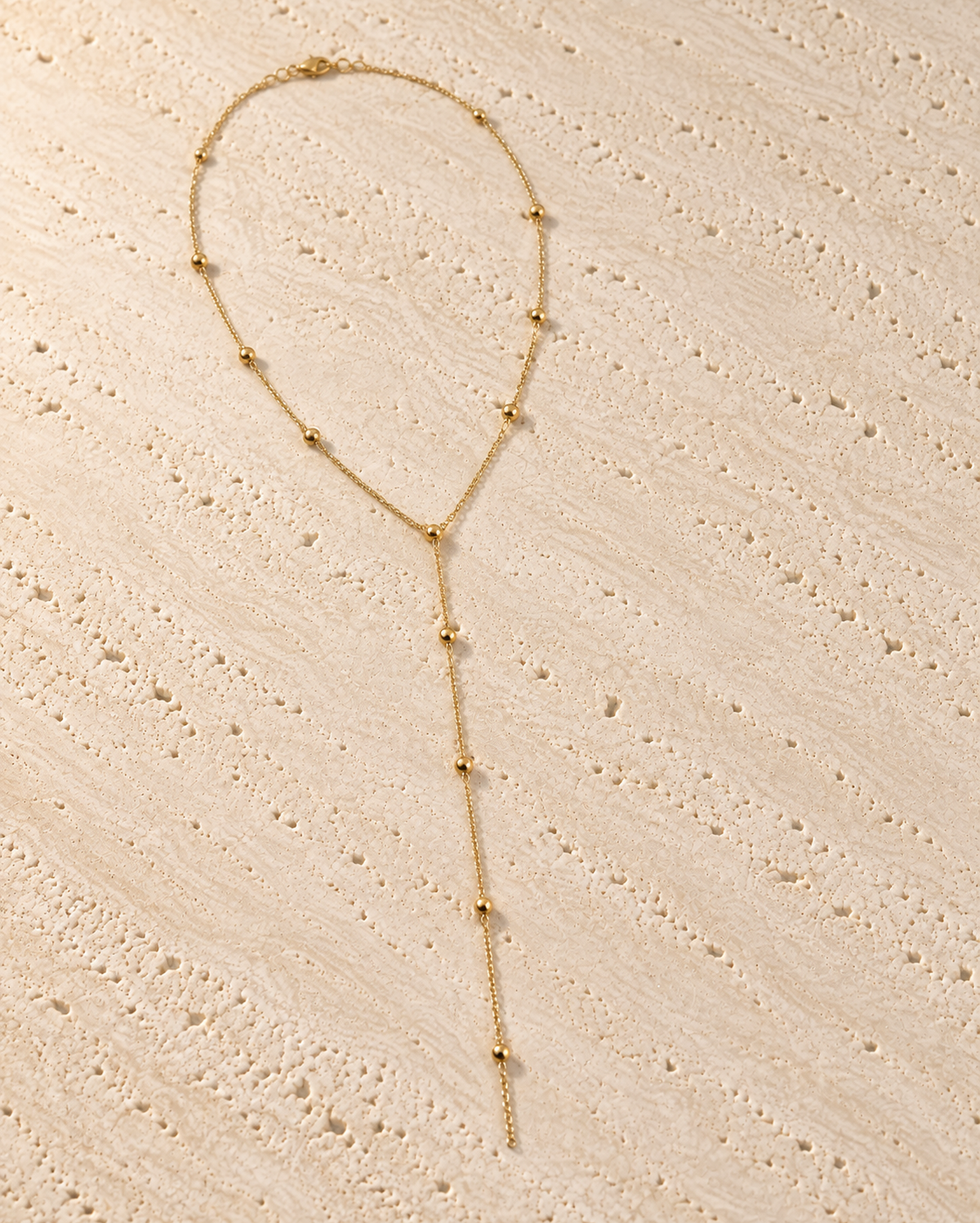 Cascata Beaded Y-Necklace in goudkleur op warm travertin