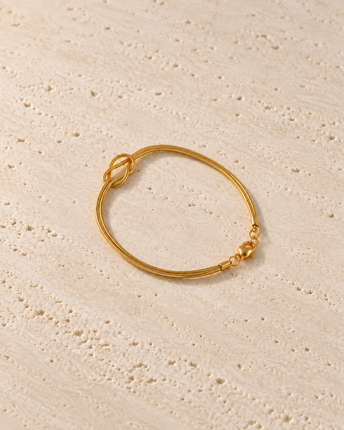 Legame Knot Bracelet in goudkleur op warm travertin