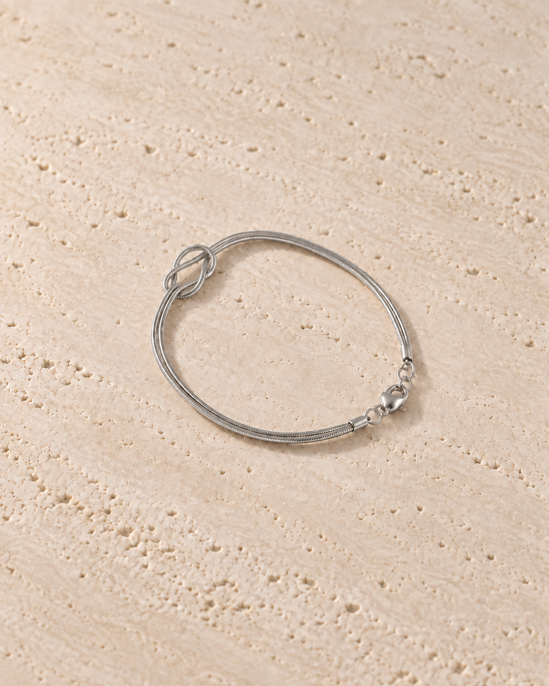 Legame Knot Bracelet in zilverkleur op warm travertin