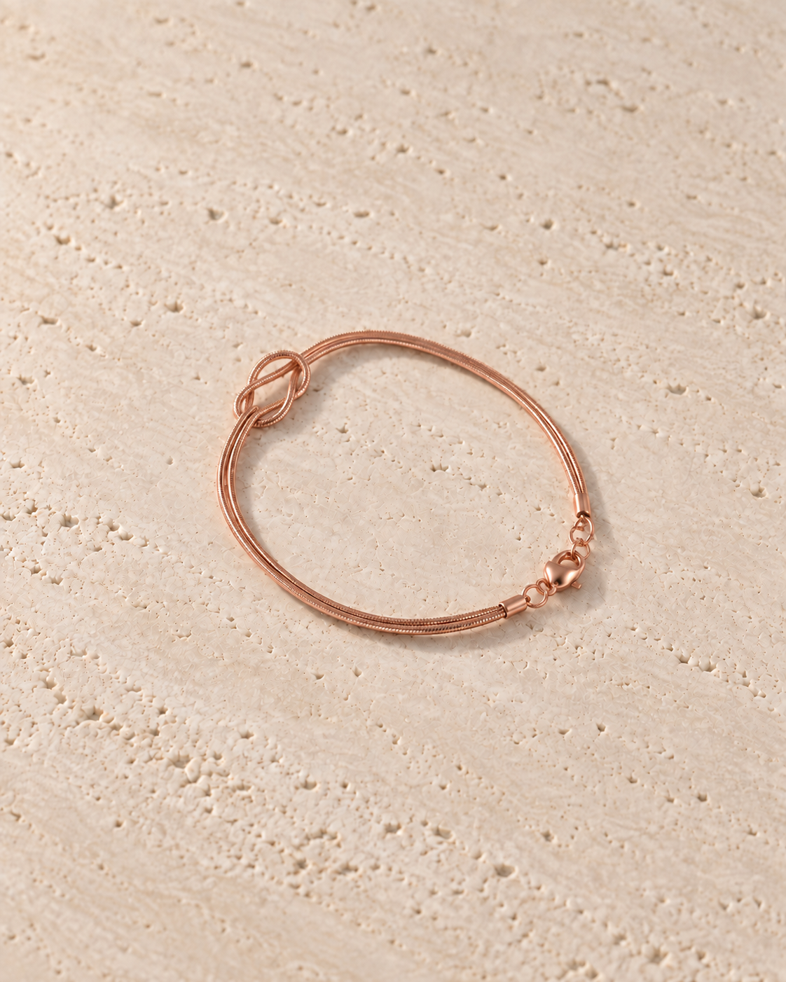 Legame Knot Bracelet in roségoudkleur op warm travertin