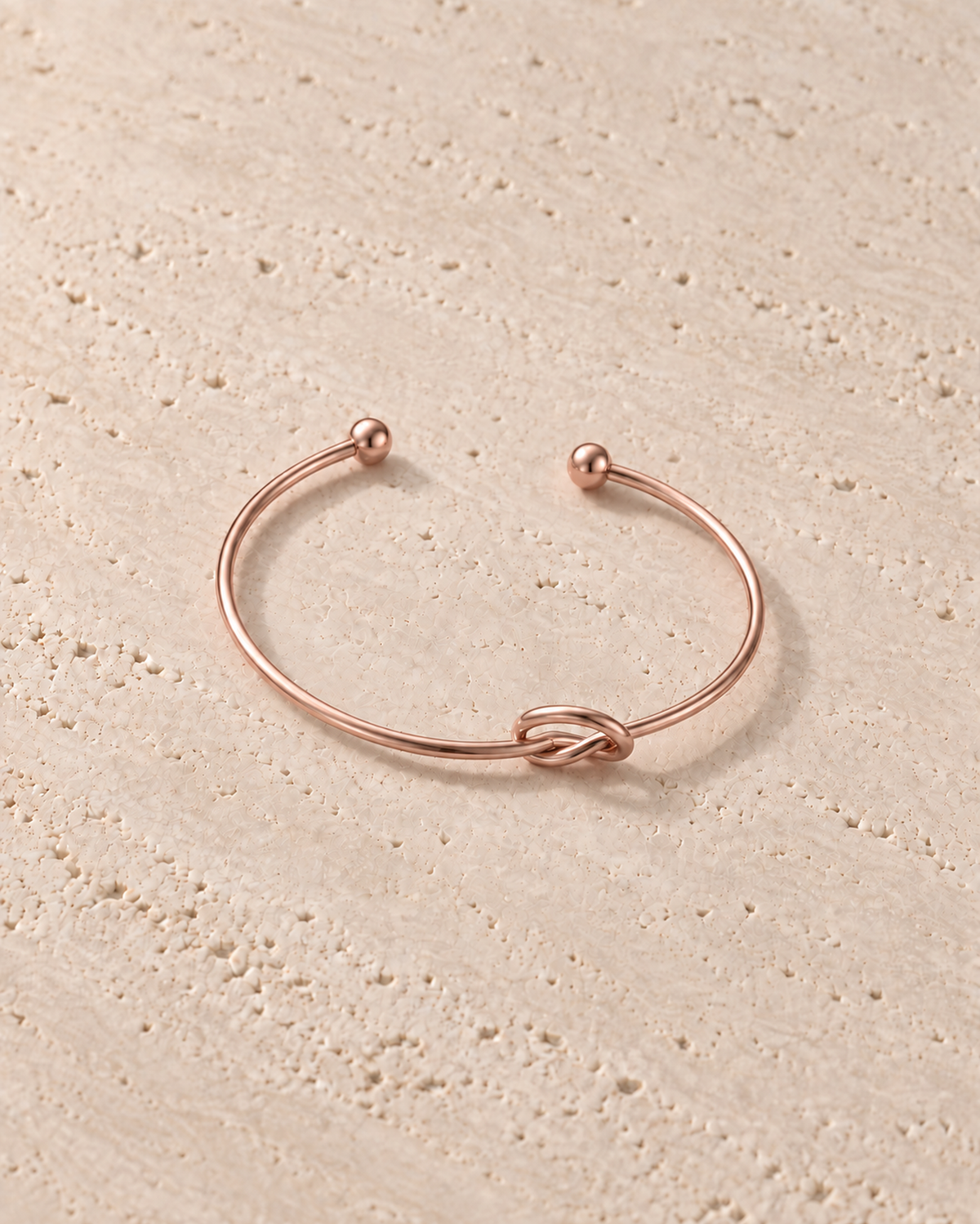 Legame Knot Cuff in goudkleur op warm travertin