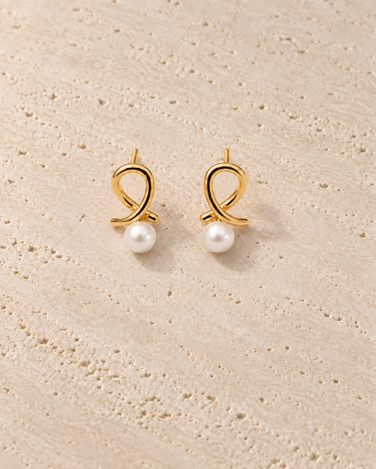 Nodo Pearl Drop Earrings in goudkleur op warm travertin
