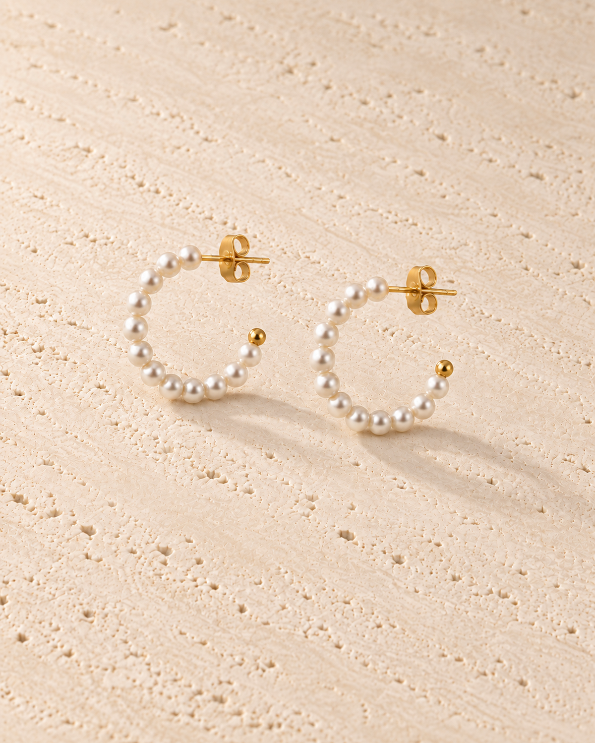 Perla Pearl Hoop Earrings in goudkleur op warm travertin